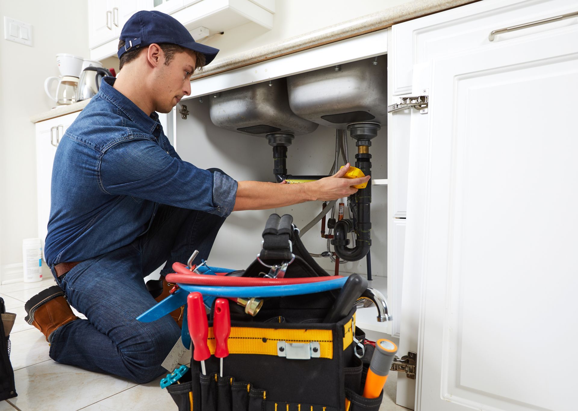 Plumber repairing pipes under a kitchen sink with tools on a cart