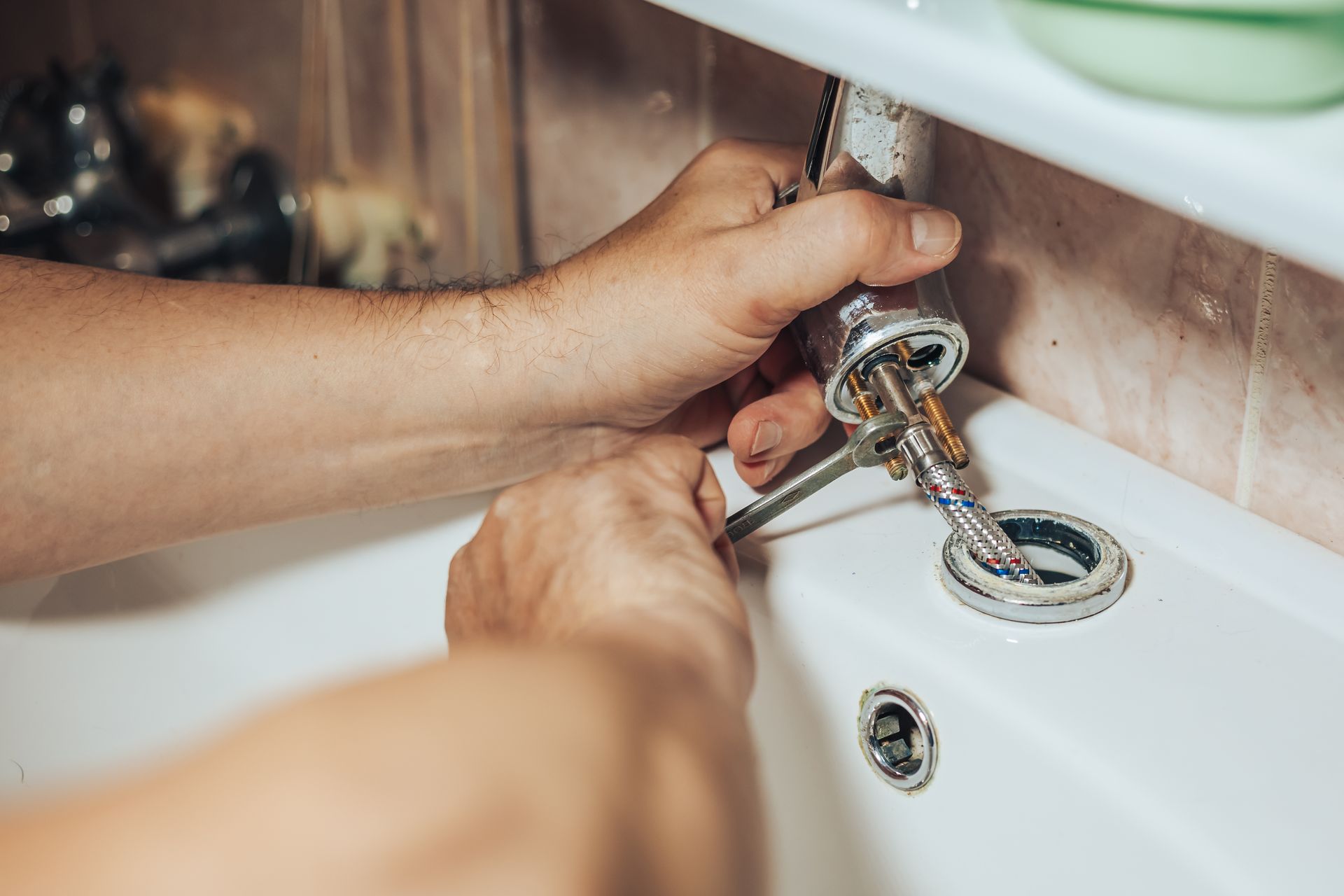 Hands repairing a bathroom sink faucet with a wrench