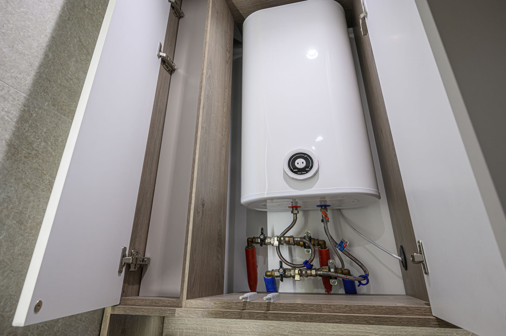 Wall-mounted white water heater in a narrow utility closet with exposed pipes and valves