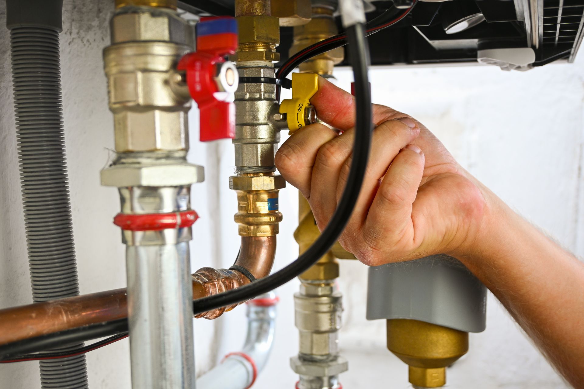 Hand tightening a brass valve on plumbing pipes under a sink with red and gray fittings