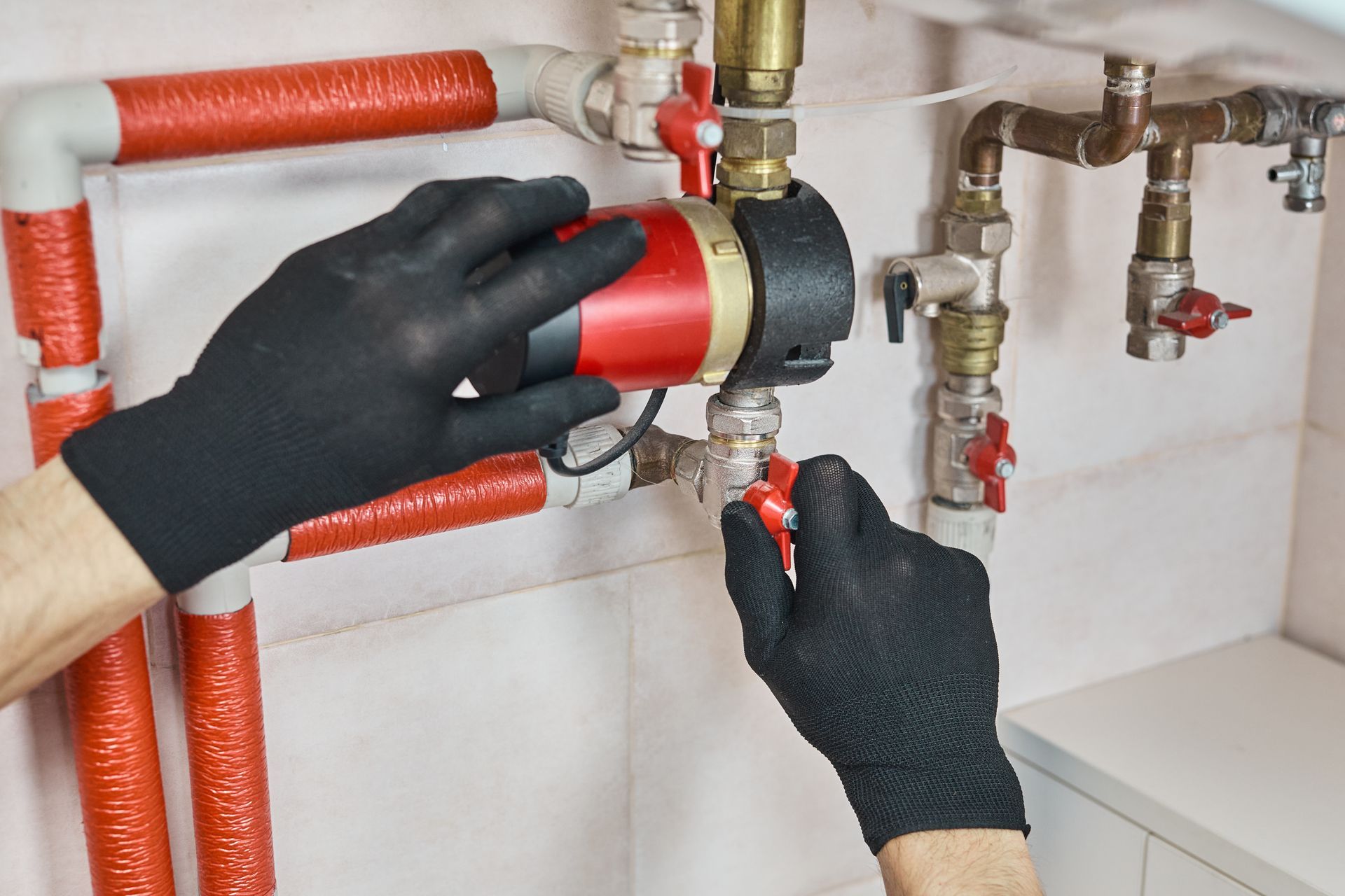 Gloved hands adjusting a red pipe fitting under a sink with exposed plumbing valves