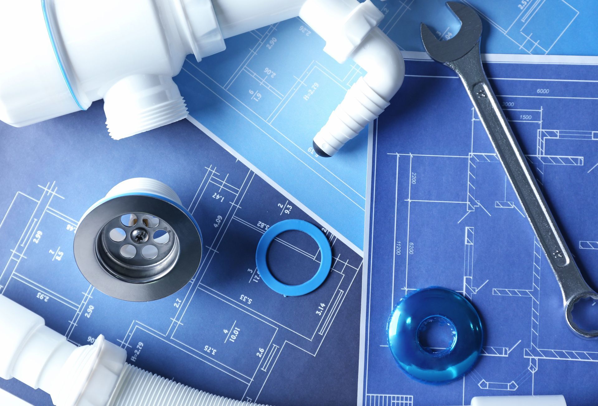Blueprints with plumbing tools and fittings, including a wrench, pipe pieces, and a faucet part