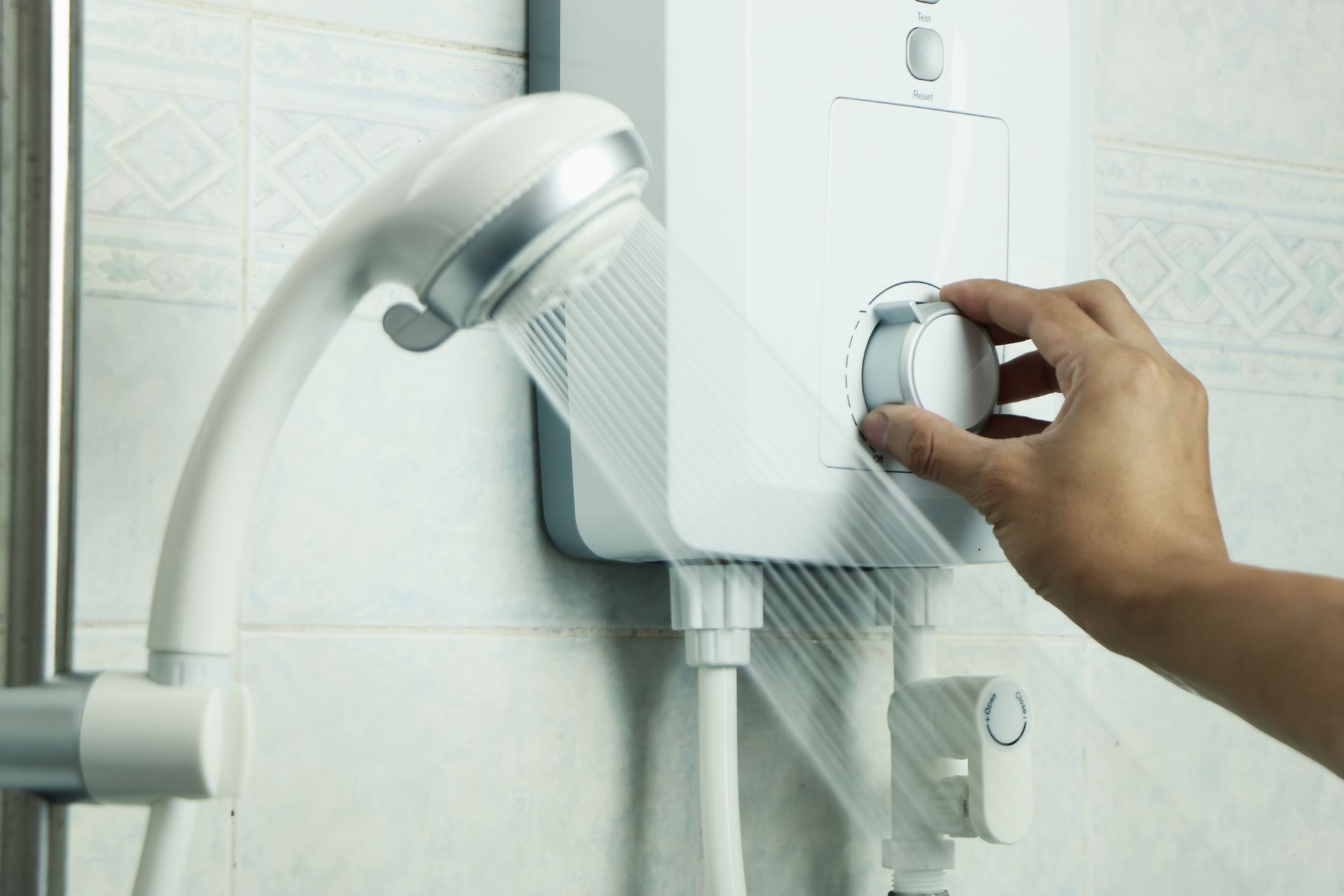 Hand adjusting a shower faucet with water running beside a handheld showerhead