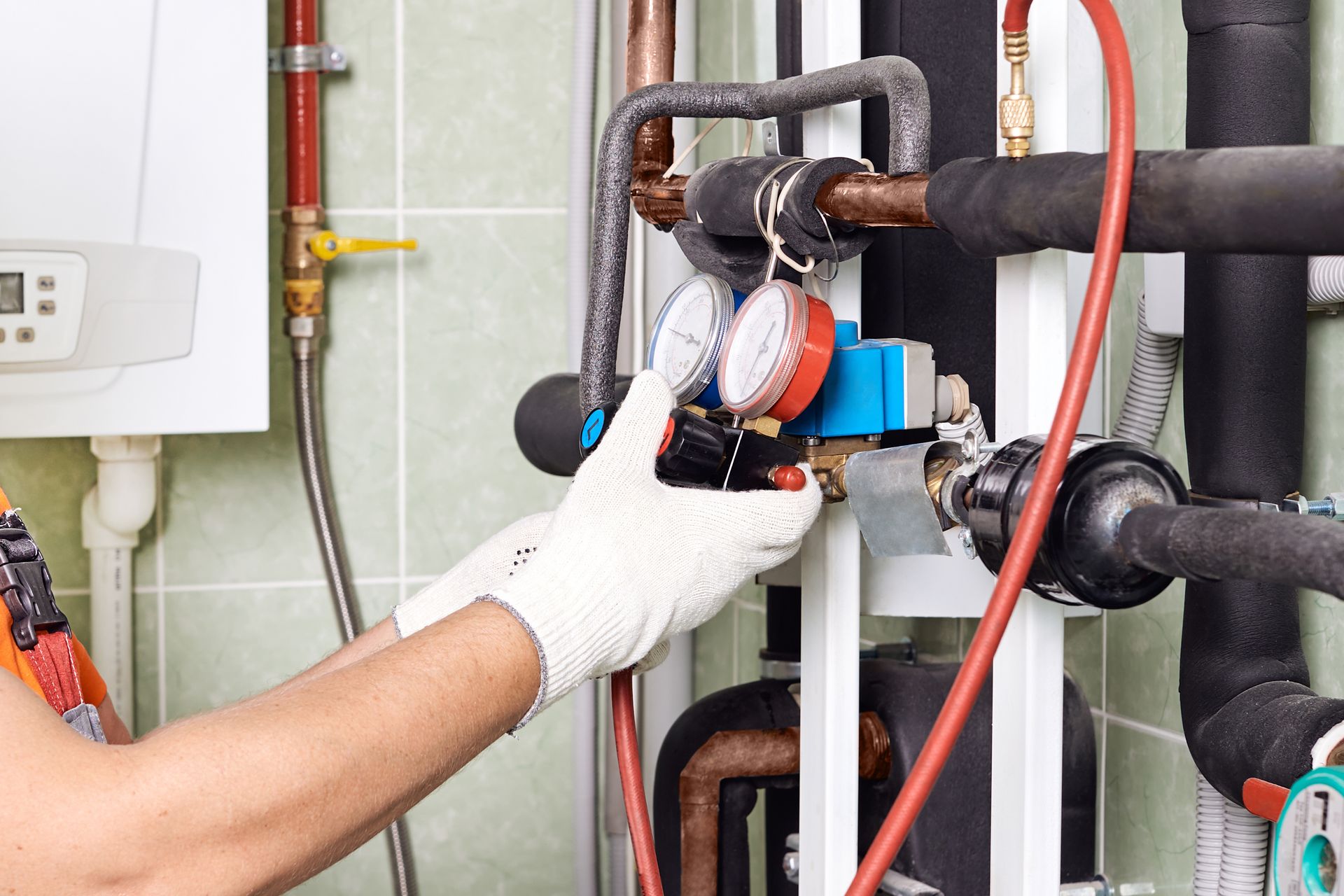 Gloved hand adjusting a gauge on industrial piping and refrigeration equipment inside a mechanical room