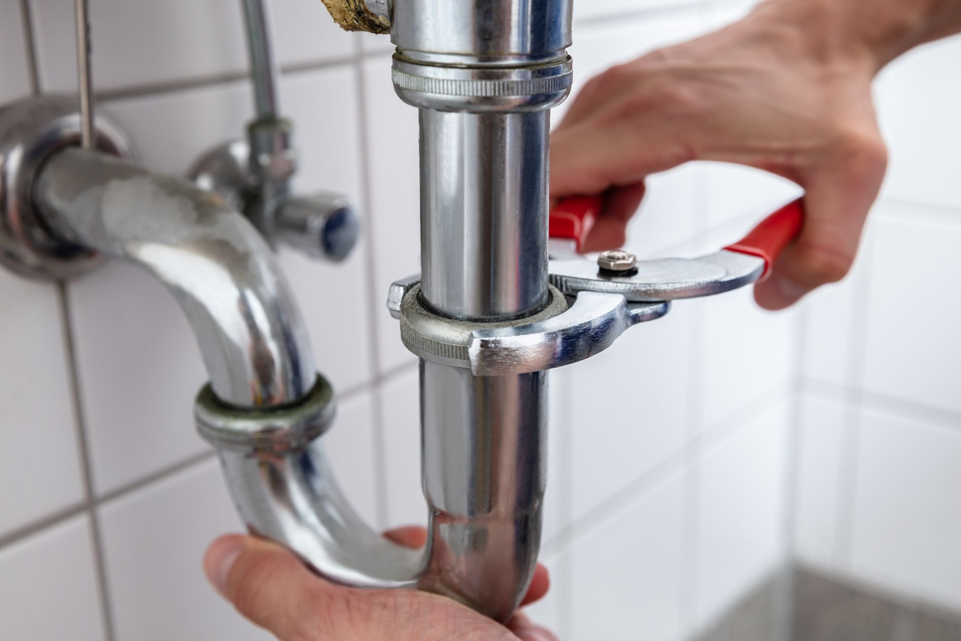 Hands using a wrench to tighten a chrome pipe under a sink