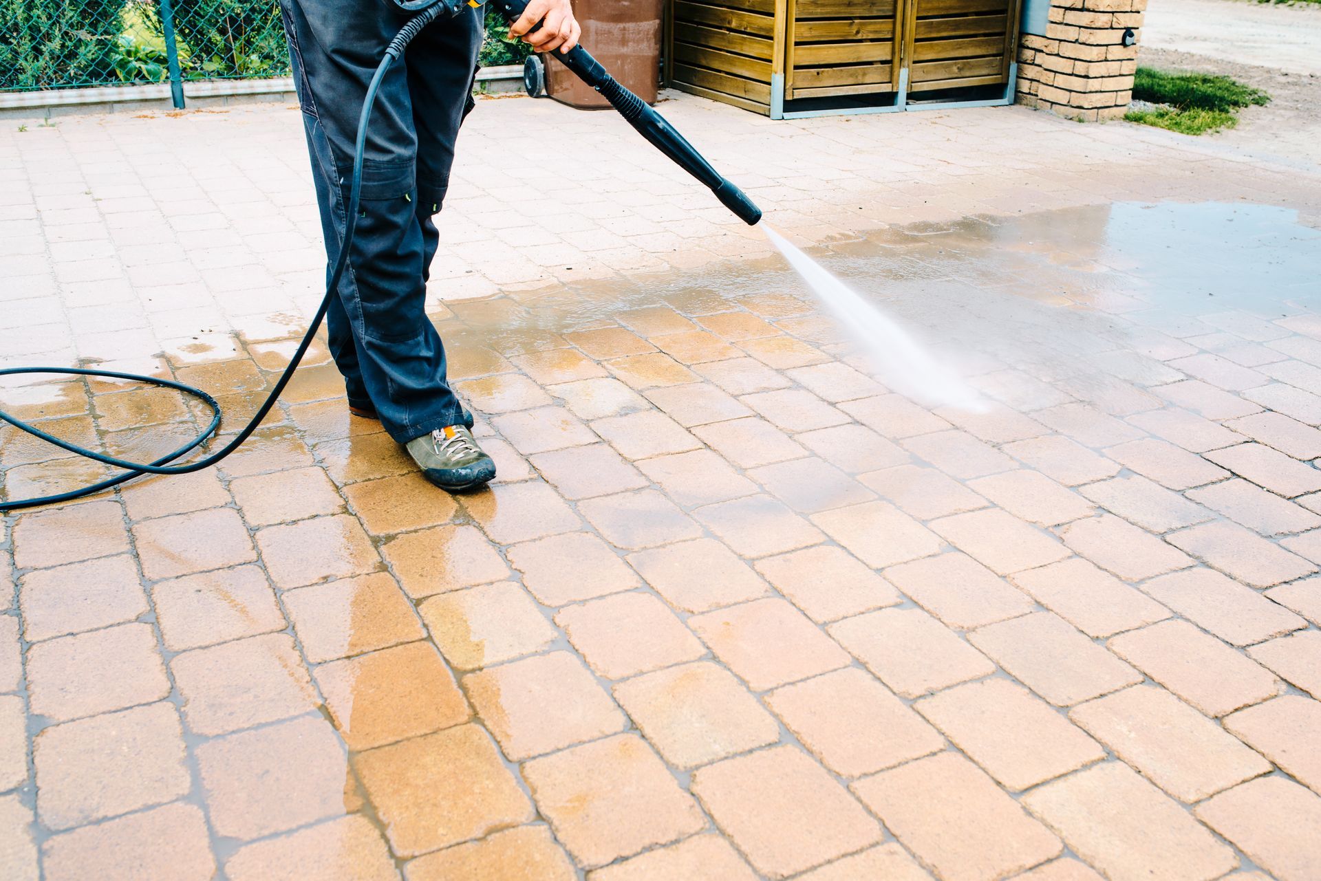 Person pressure-washes a brick patio with a hose.