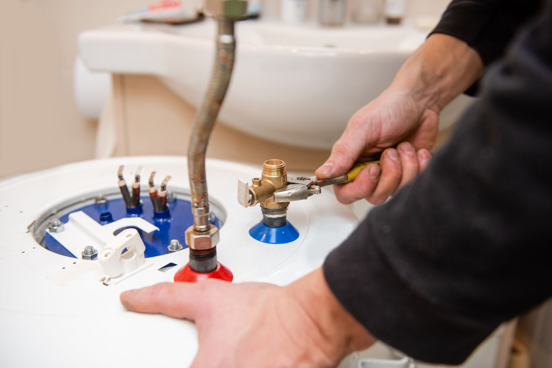Technician repairing a sink fixture with tools under a white basin