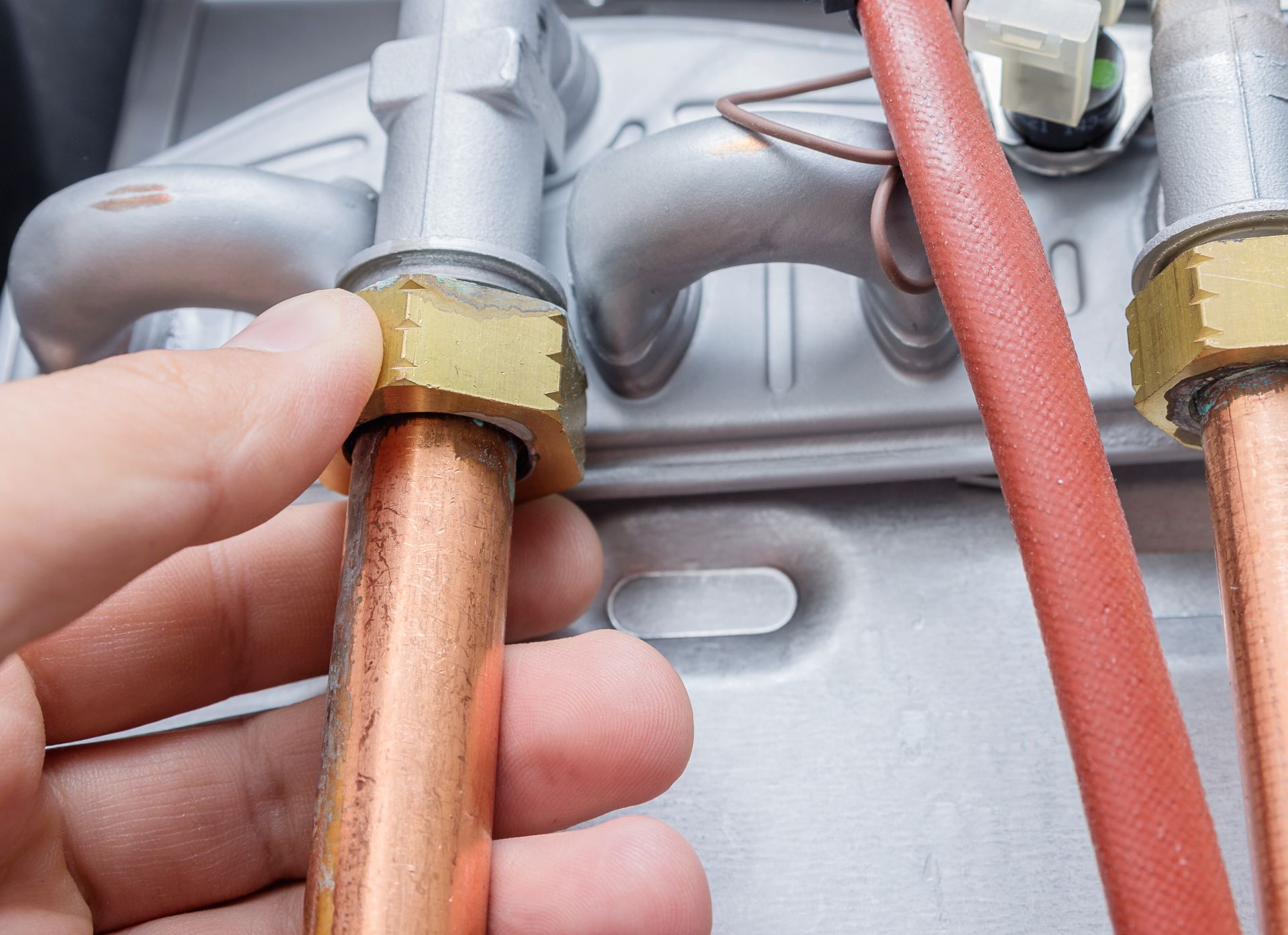 Hand tightening a brass fitting on a copper pipe beside red insulated tubing