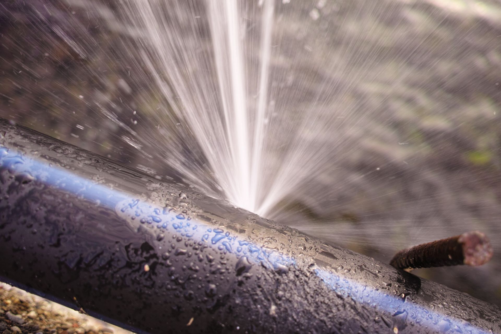 Water spraying from a hose onto a wet dark pipe outdoors