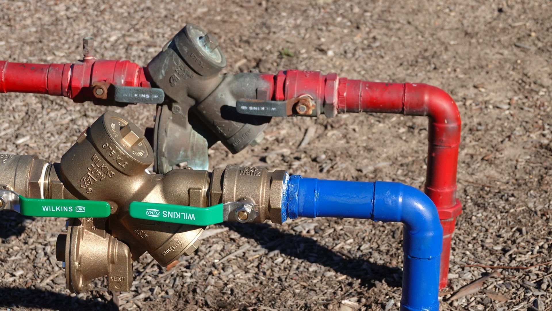 Color-coded industrial pipes and valves on dry ground, with red, blue, and green sections.