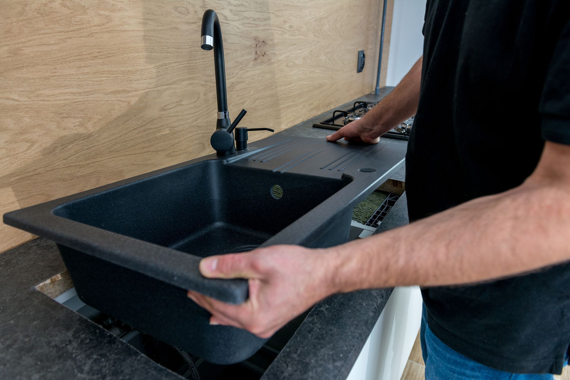 Person installing a black rectangular sink on a countertop next to a faucet