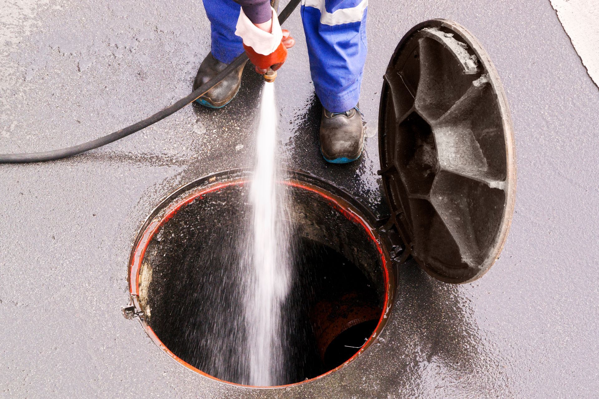 Worker using a pressure washer to clean a manhole on wet pavement