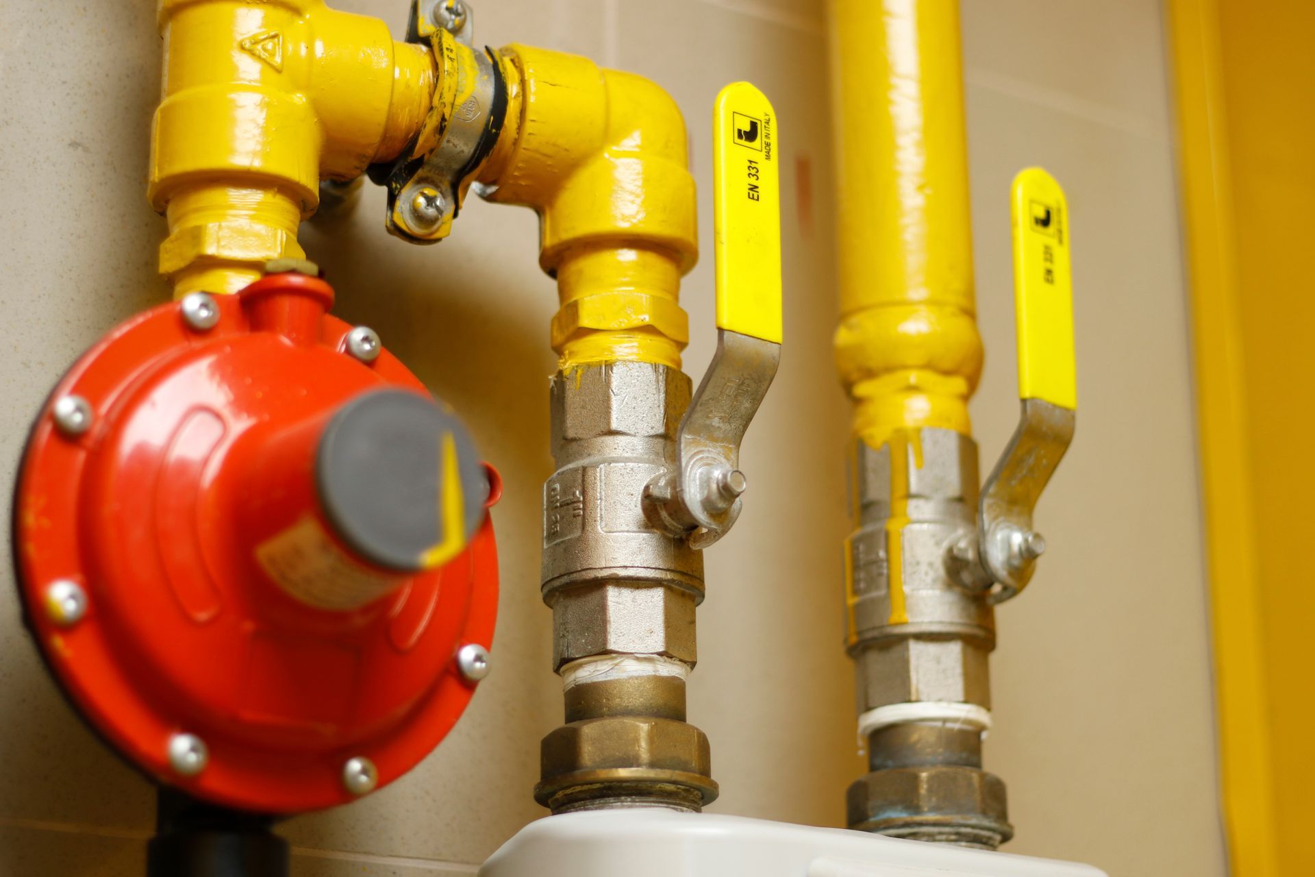 Yellow gas pipes and red valve regulator in a utility room, close-up.