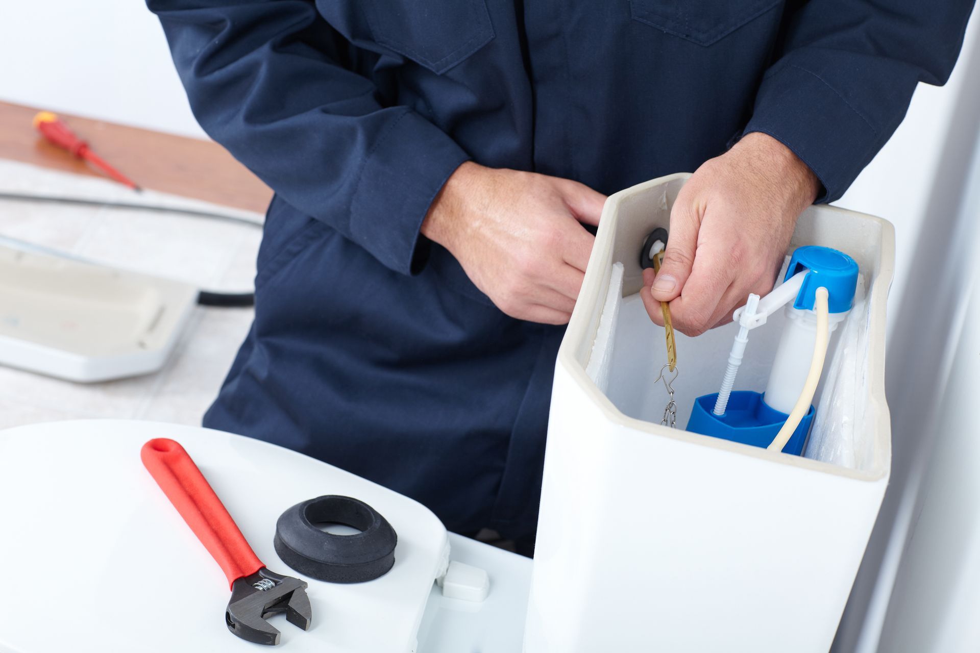 Person repairing a toilet tank with tools on a white workbench