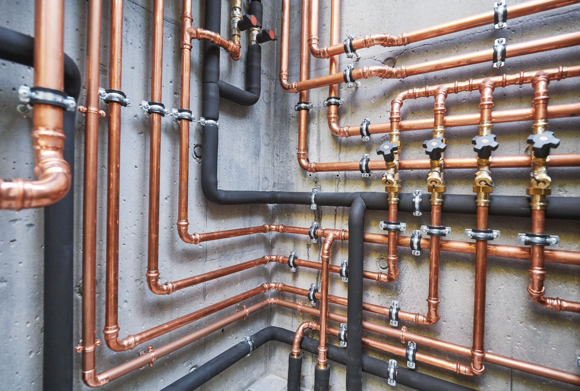 Copper and black plumbing pipes arranged on a gray wall with multiple bends and valves