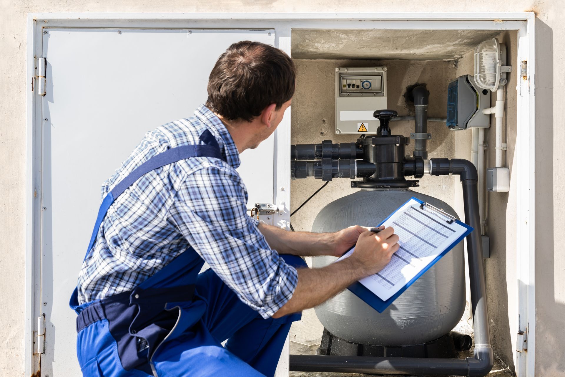 Technician inspecting boiler equipment and recording notes on a clipboard inside a utility cabinet
