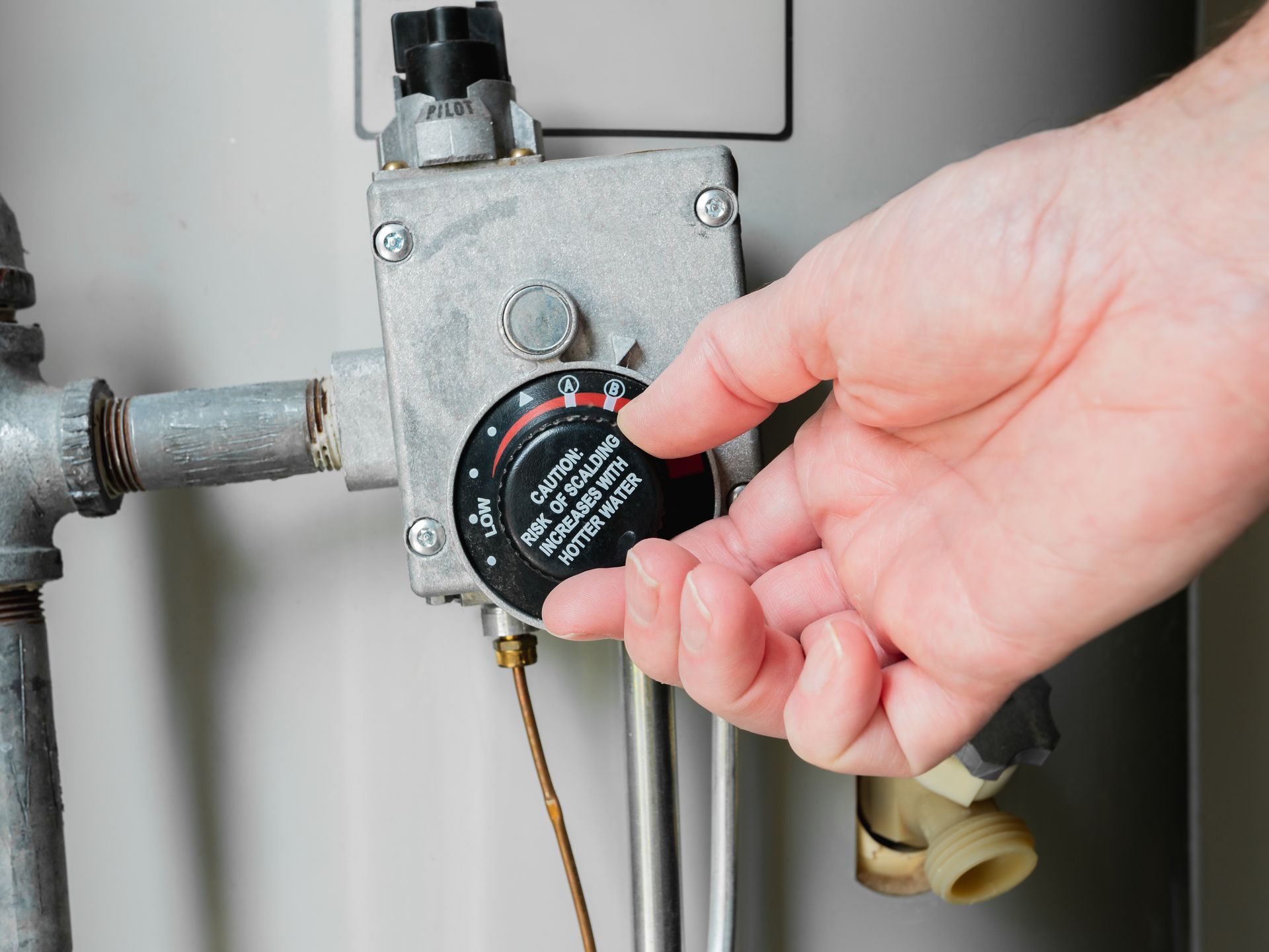Hand adjusting a water heater thermostat knob on a metal valve assembly