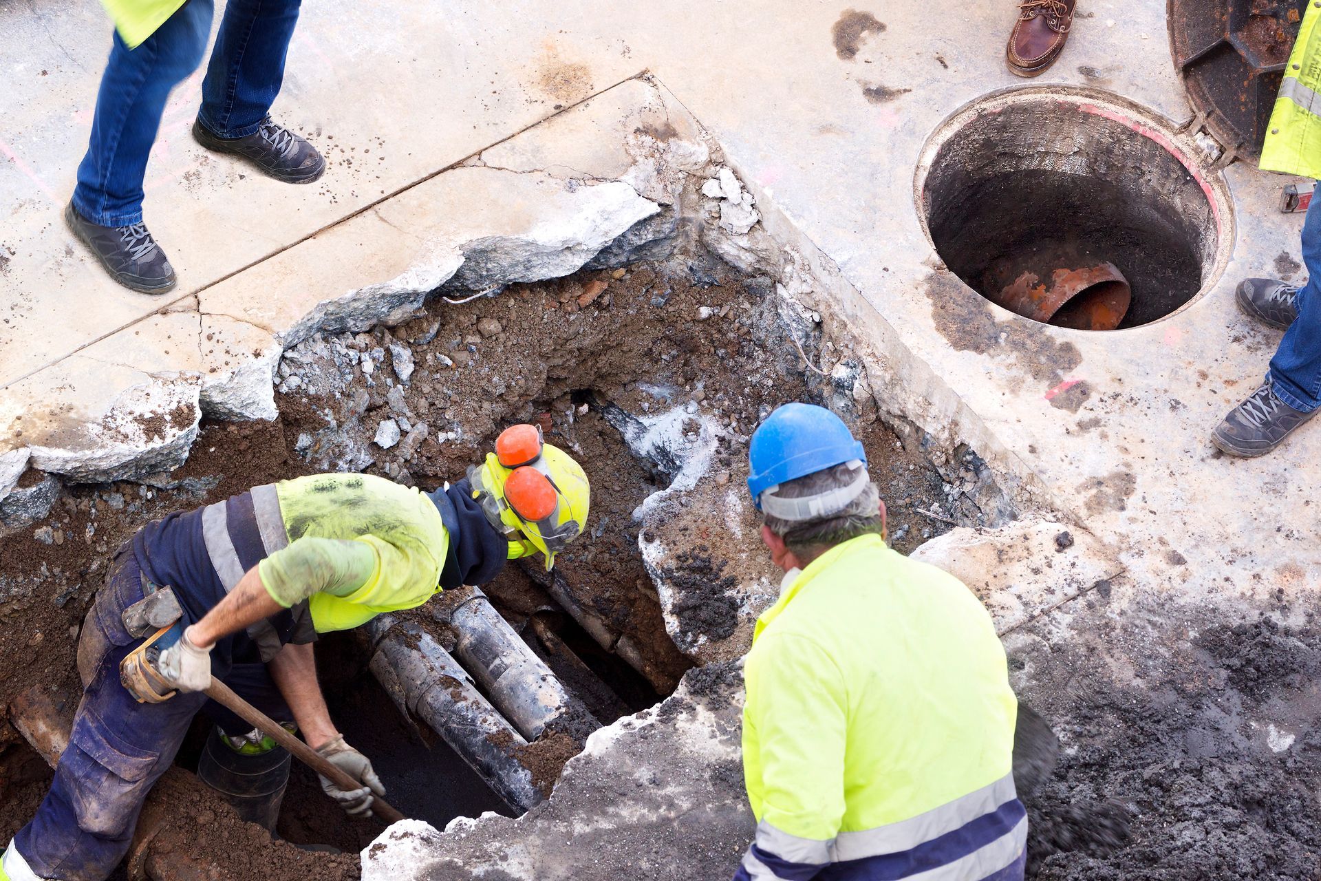 Workers in hard hats repairing a damaged underground pipe in a road excavation