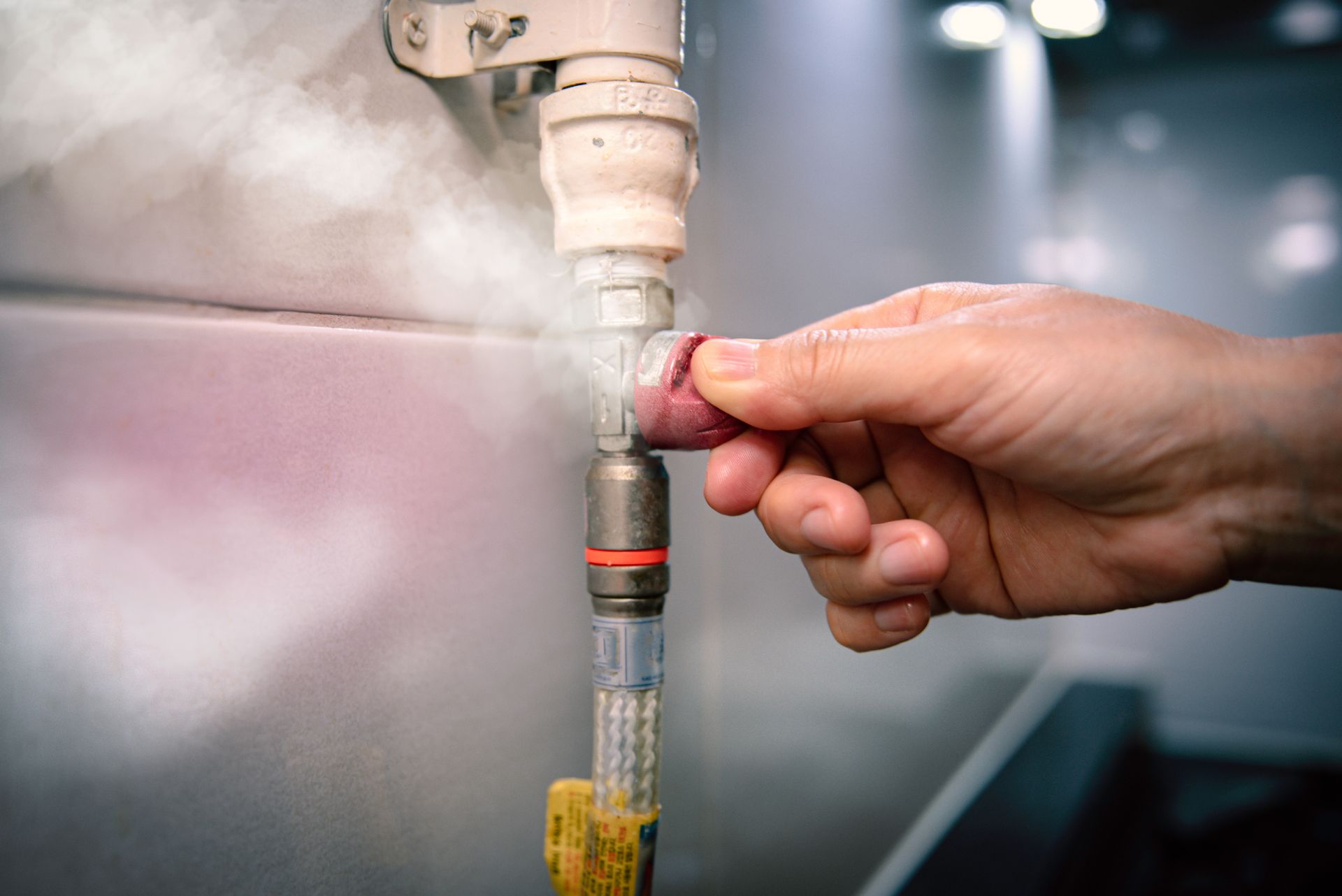 Hand holding a spray nozzle against a blurred industrial machine, mist spraying around it