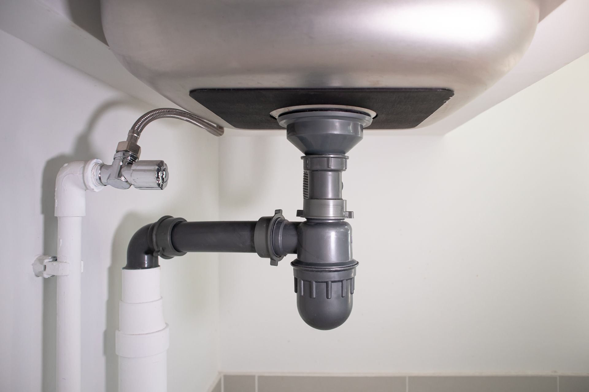 Under-sink plumbing with white drain pipes and a gray P-trap beneath a sink basin