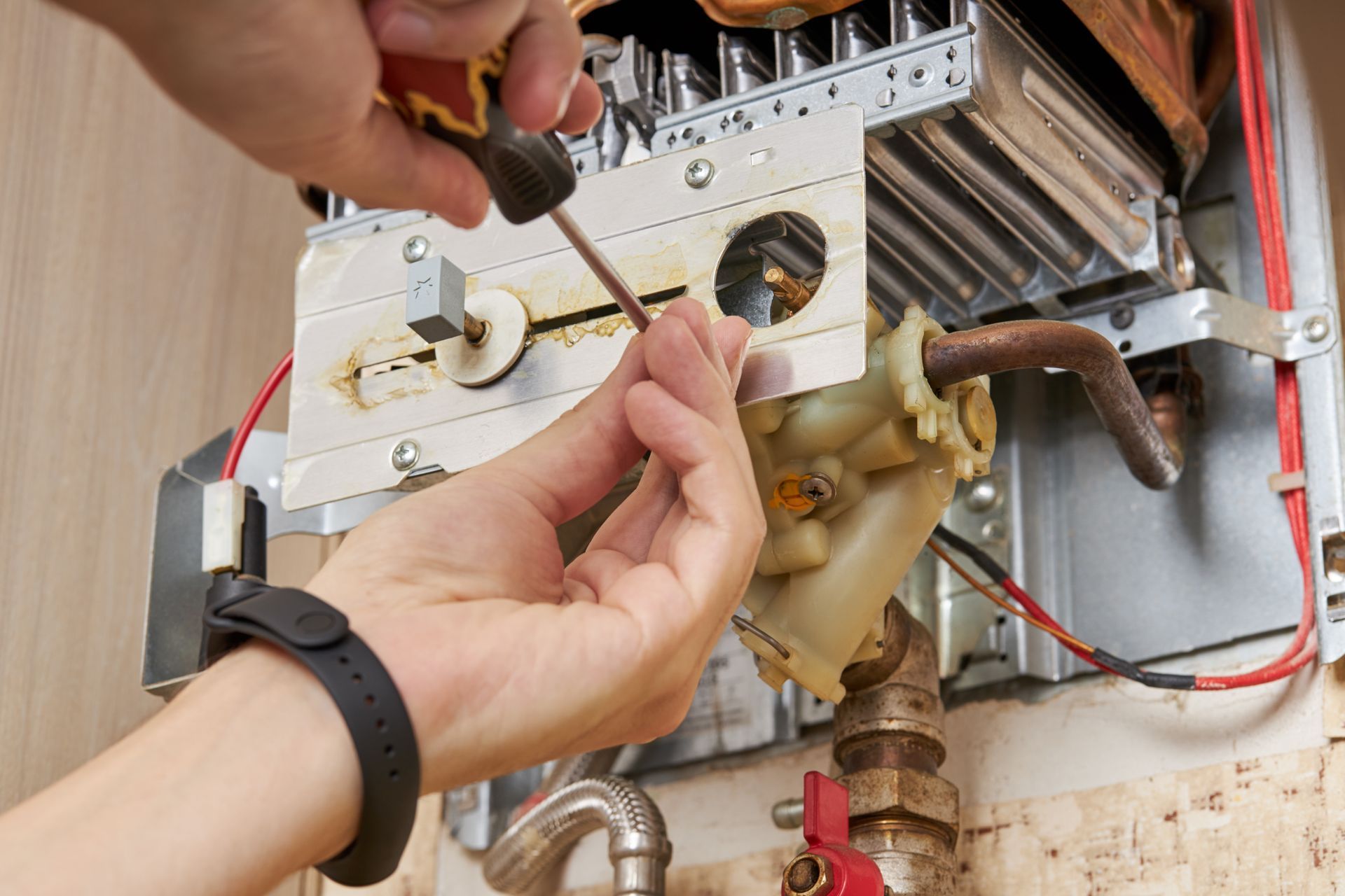 Hands adjusting a boiler control panel with wires and tools during repair work