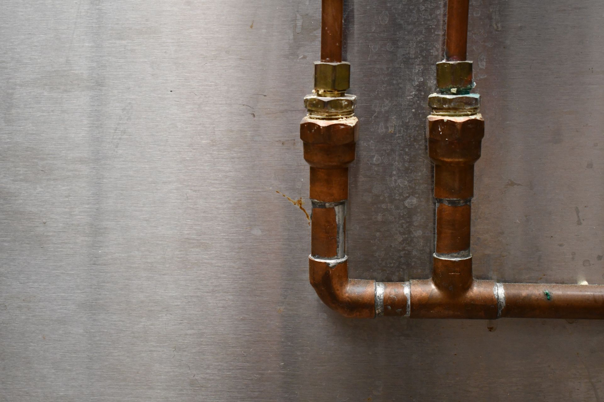 Copper pipes and brass fittings against a gray wall, with two vertical pipes joining a horizontal run.