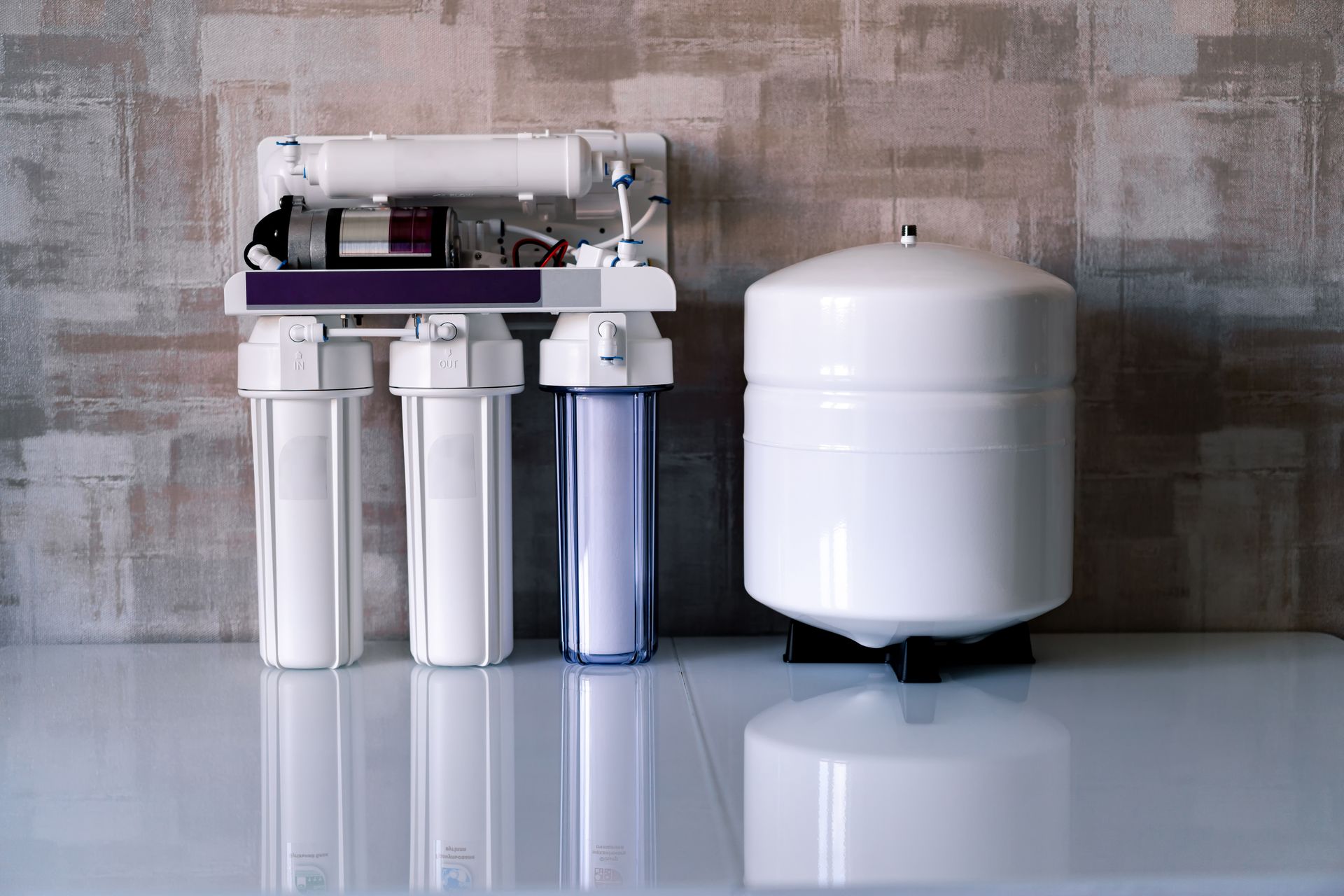 Water filter system with white canisters and a storage tank on a reflective floor against a concrete wall