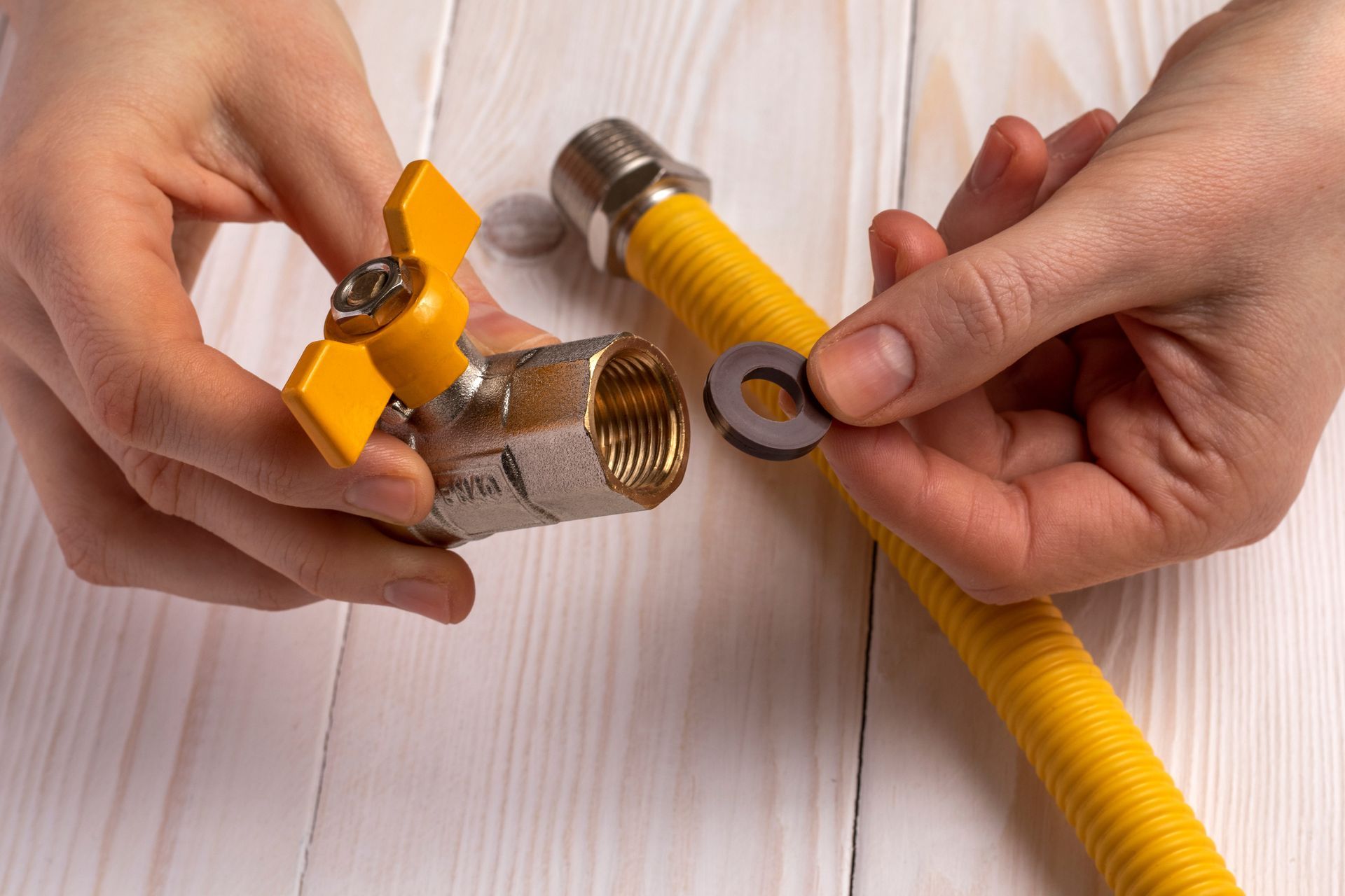 Hands connecting yellow gas hose fittings with tools on a light wooden table.