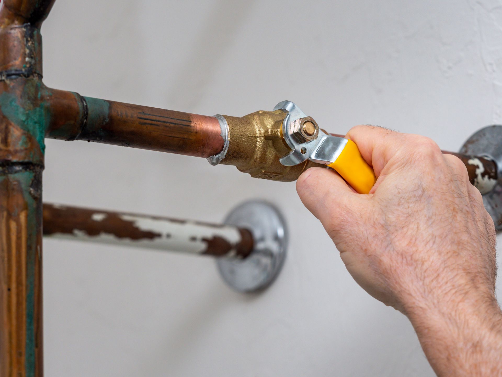 Hand turning a yellow valve handle on a copper pipe under a sink