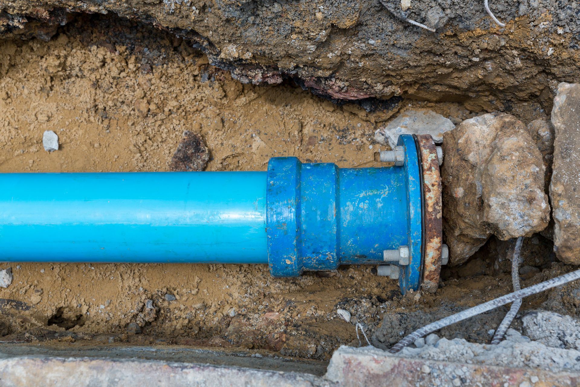 Blue plastic pipe connected to a larger fitting in a dirt trench beside rocks