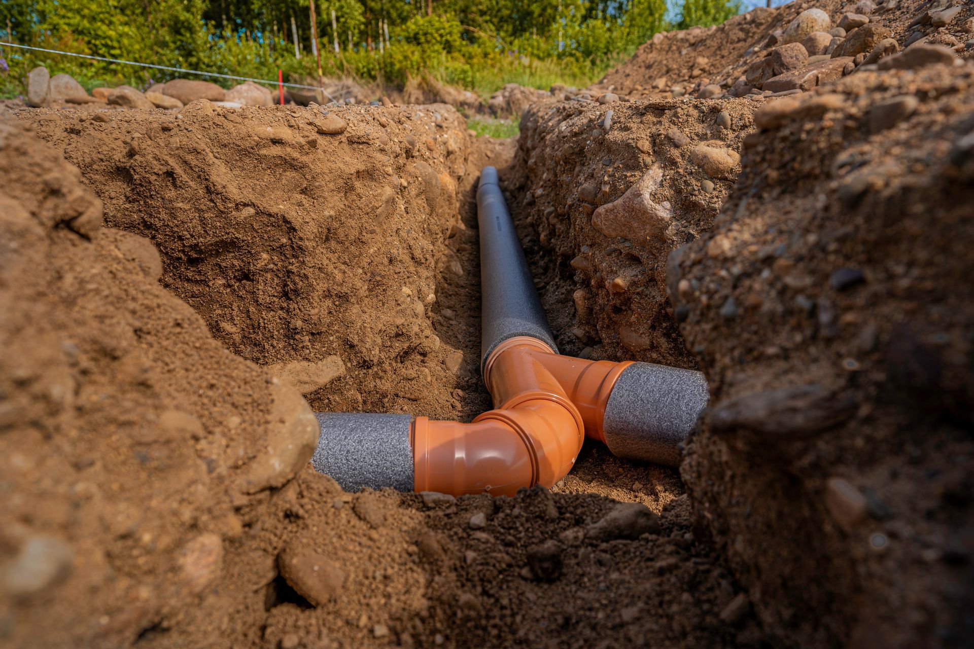Orange PVC pipes connected in a dirt trench during underground utility installation