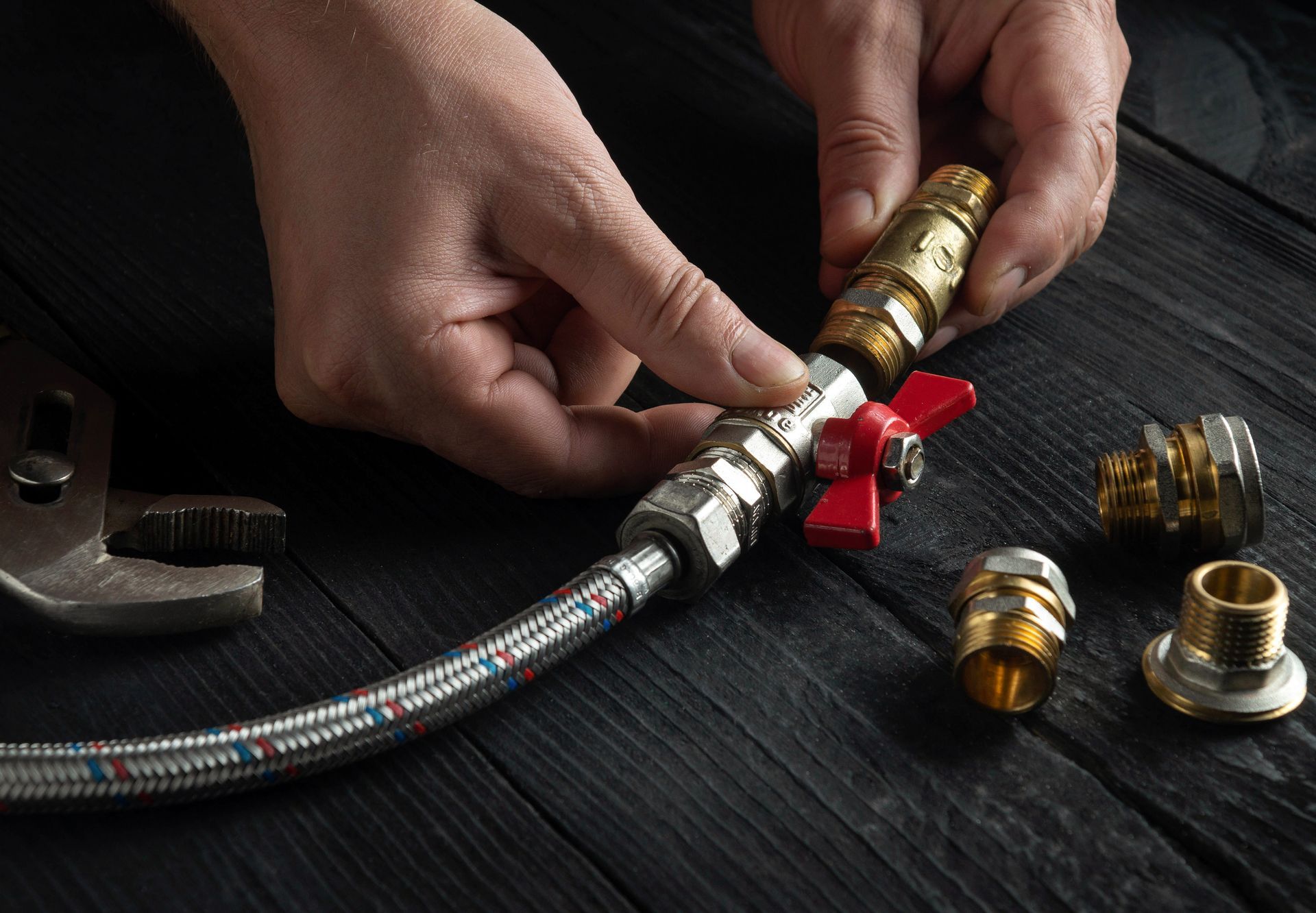 Hands connecting metal hose fittings on a dark wooden surface, with tools and brass connectors nearby