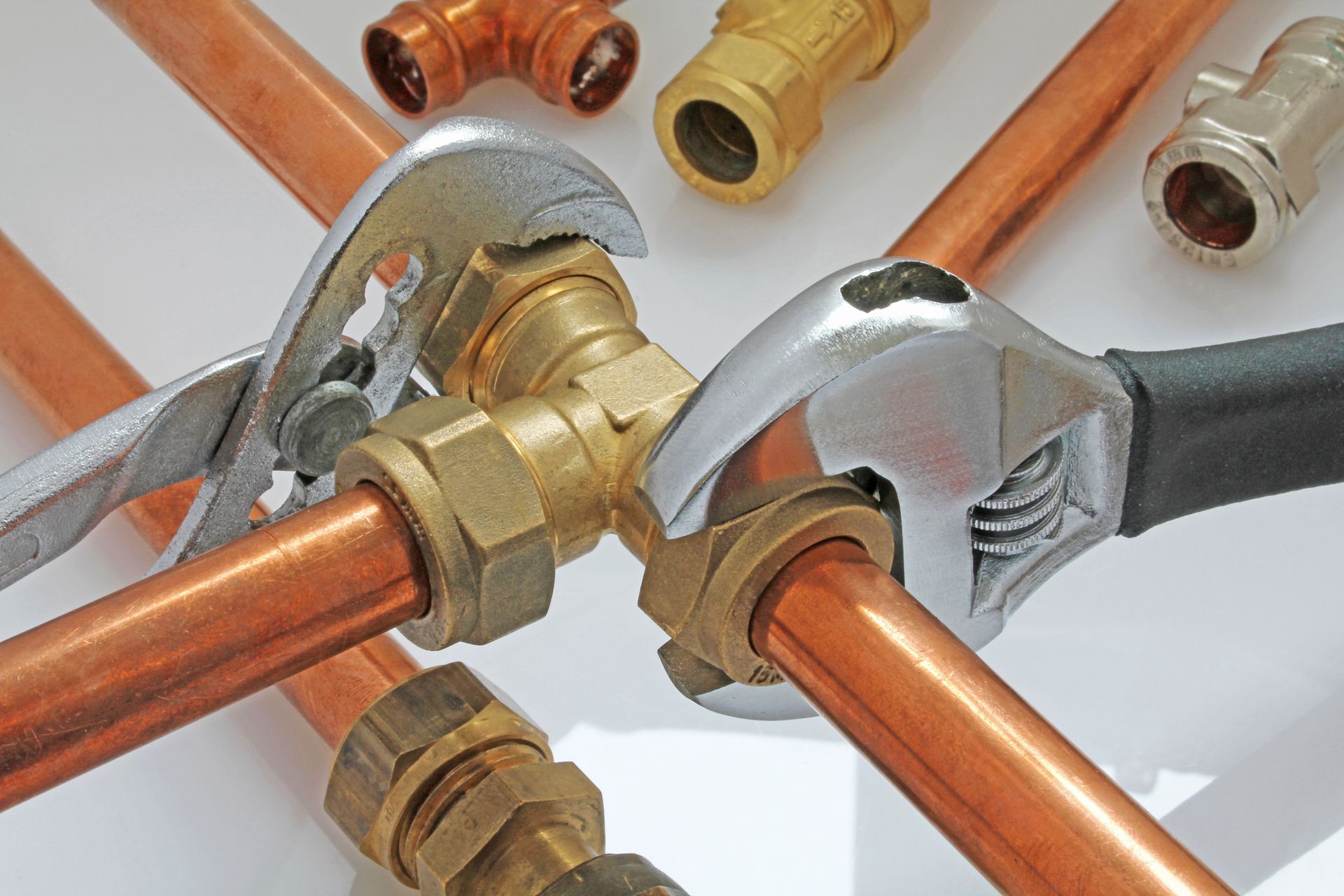 Close-up of copper pipes and metal plumbing fittings connected with wrenches on a white surface