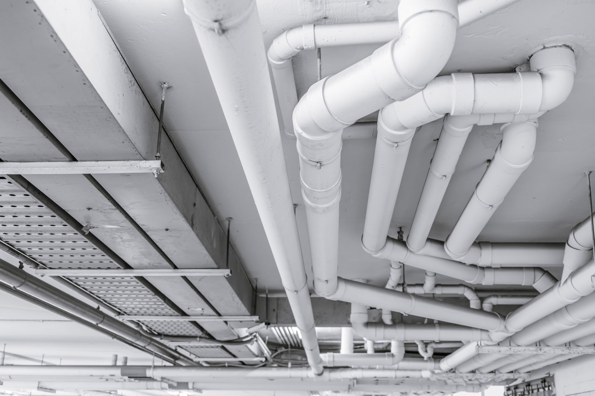 White industrial pipes and ductwork running across a ceiling in a building interior.