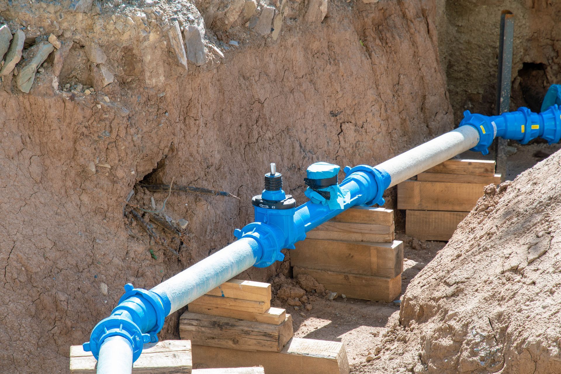 Blue pipeline with valves running through a dirt trench at a construction site