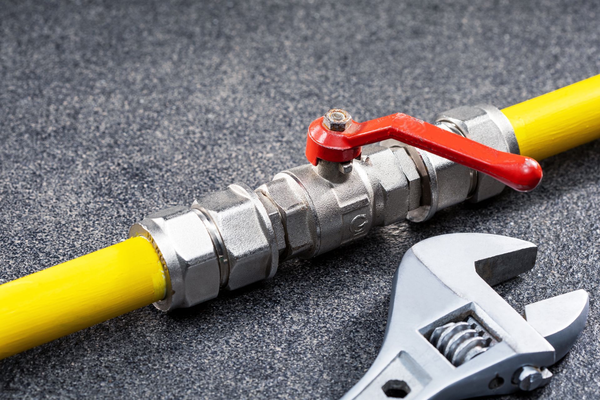 Yellow gas pipe with metal shutoff valve and wrench on a gray surface