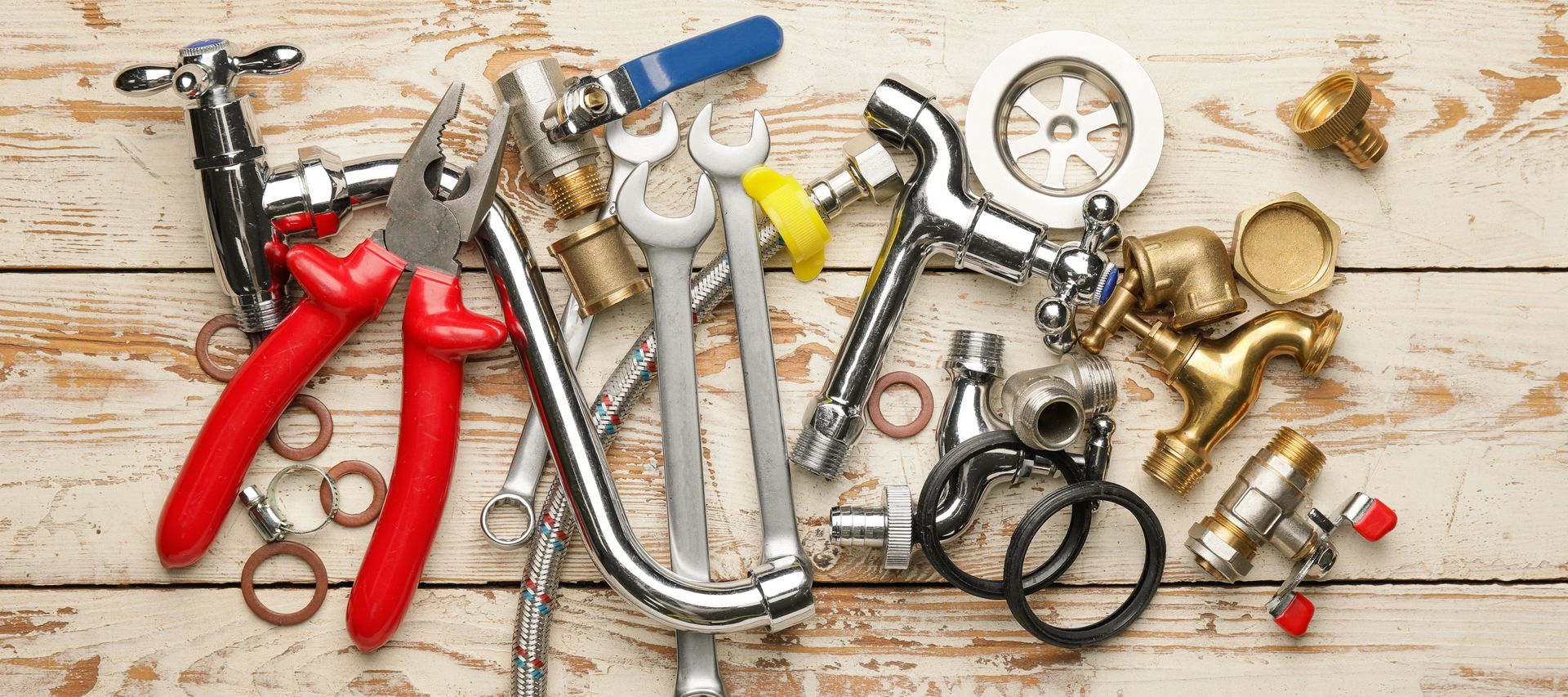 Assorted plumbing tools and fittings arranged on a wooden surface, including wrenches, pliers, and pipes