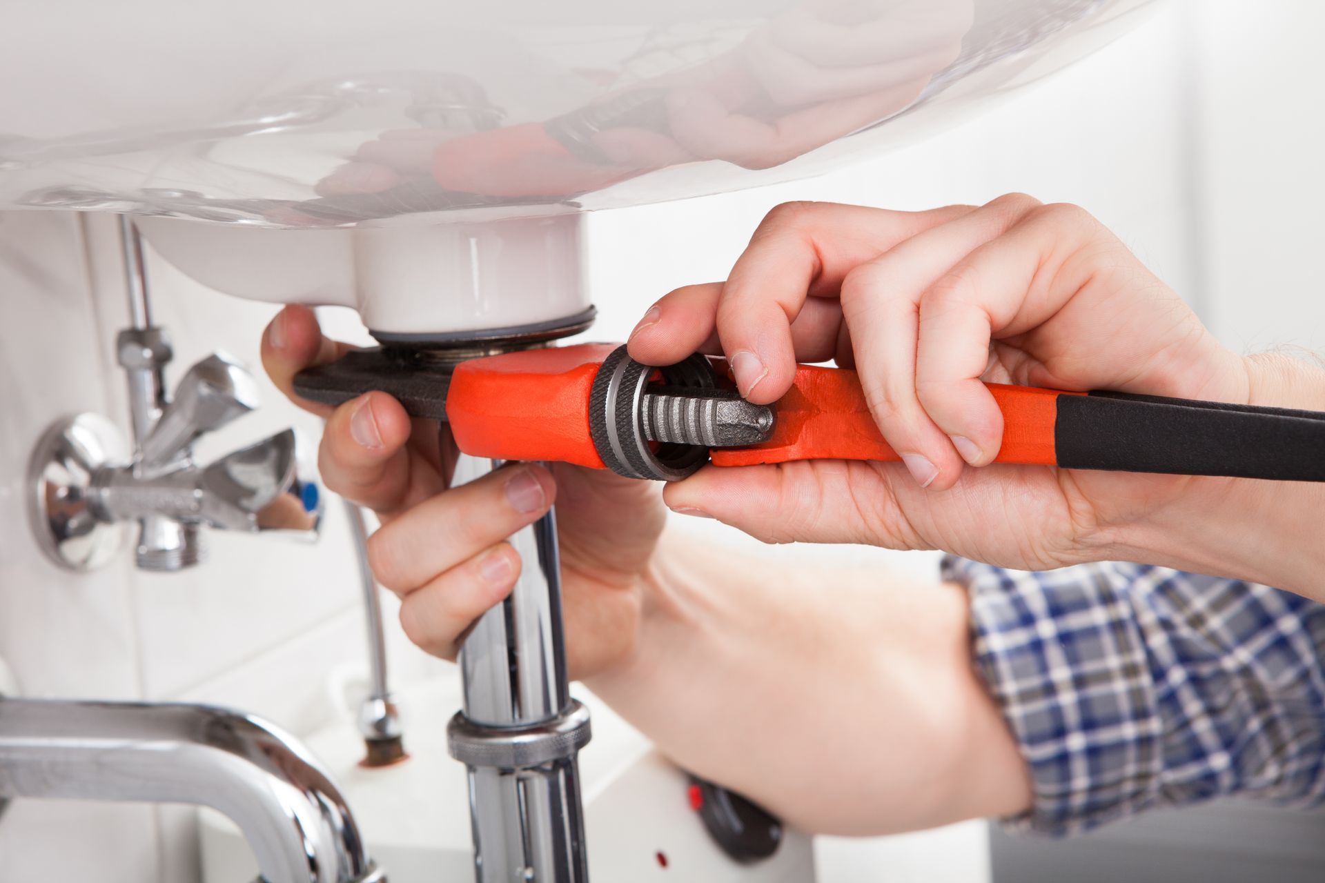 Hands tightening a red pipe wrench on a sink drain under a bathroom sink