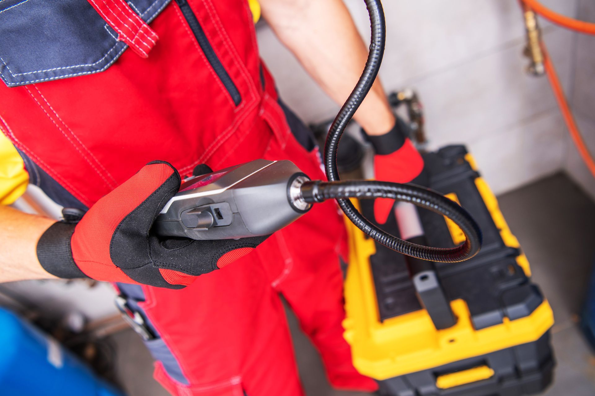 Technician in red overalls using a crimping tool near a yellow toolbox and cables
