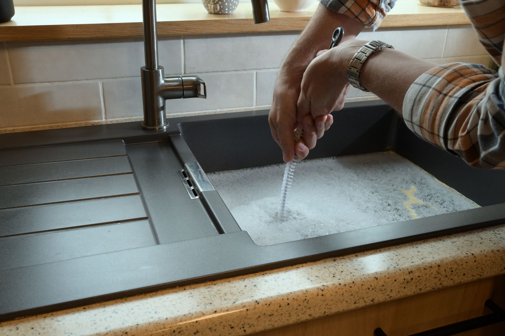 Hands washing under a kitchen faucet in a stainless steel sink beside a window.