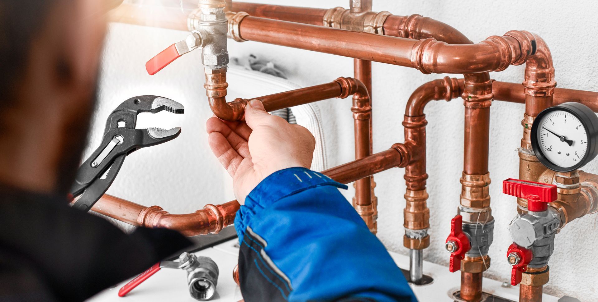 Technician adjusting copper pipes and valves with a pressure gauge in a utility room