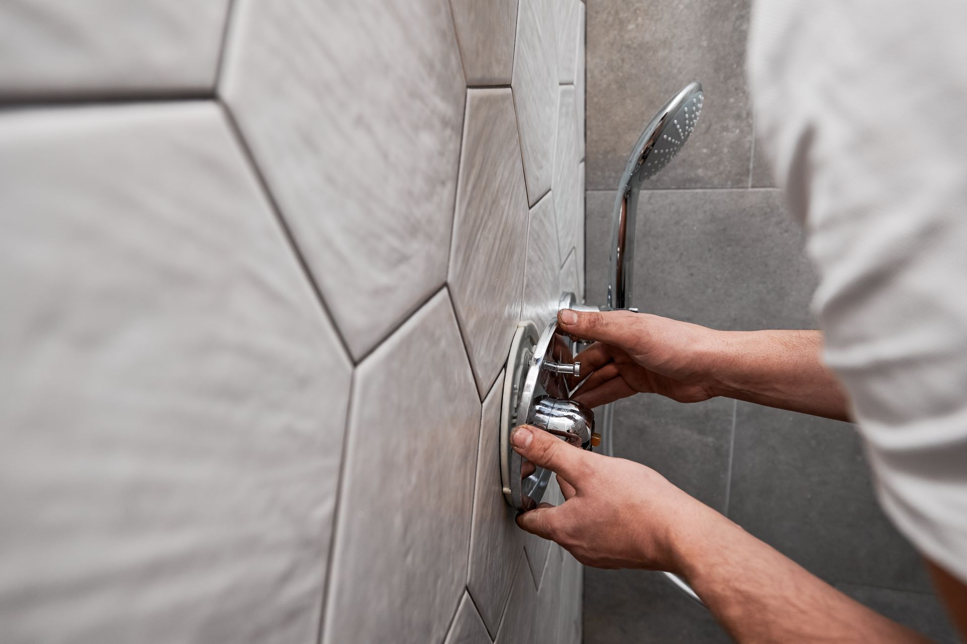 Hands installing a silver shower fixture on a tiled bathroom wall.