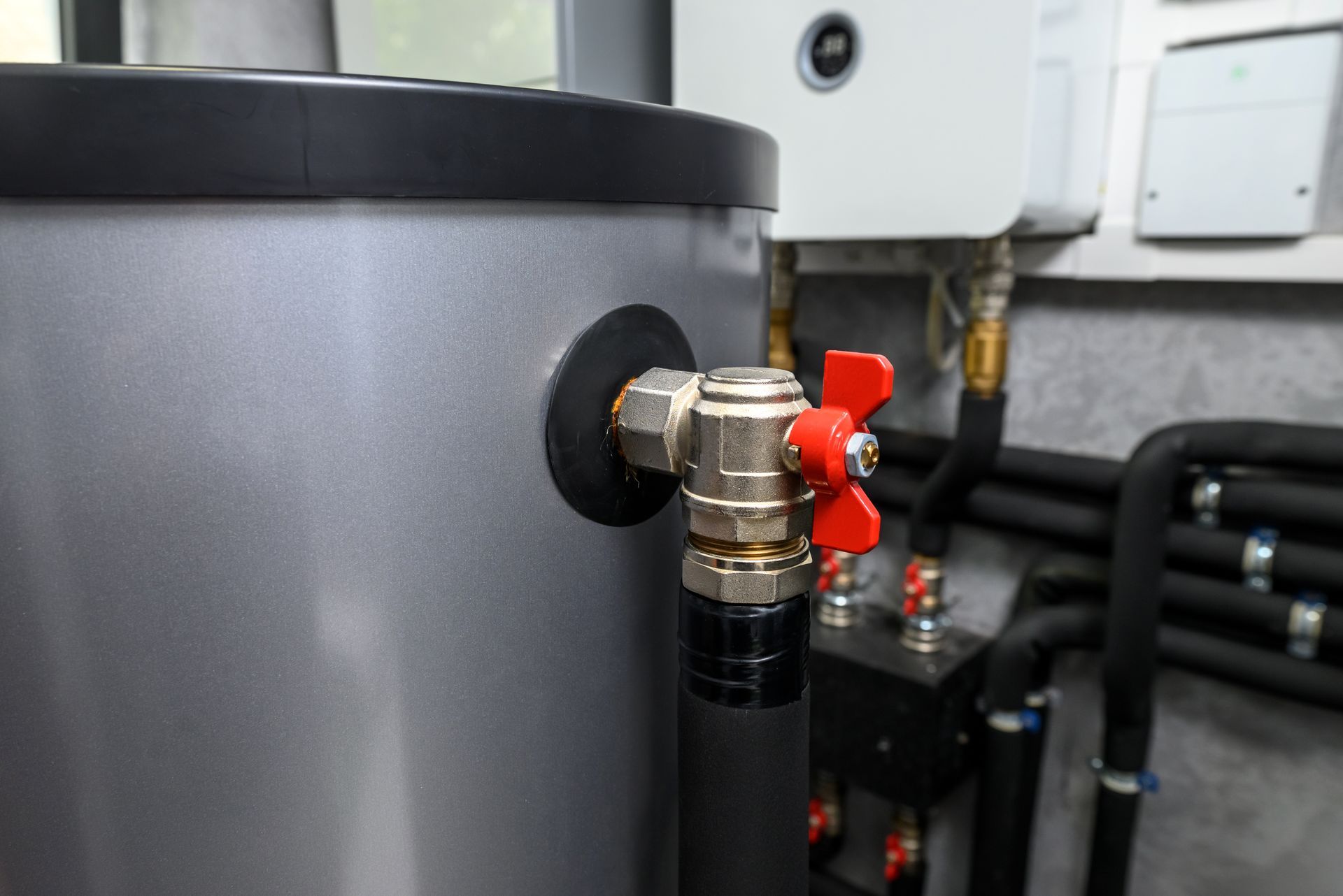 Close-up of a gray tank valve with a red handle in an industrial room.