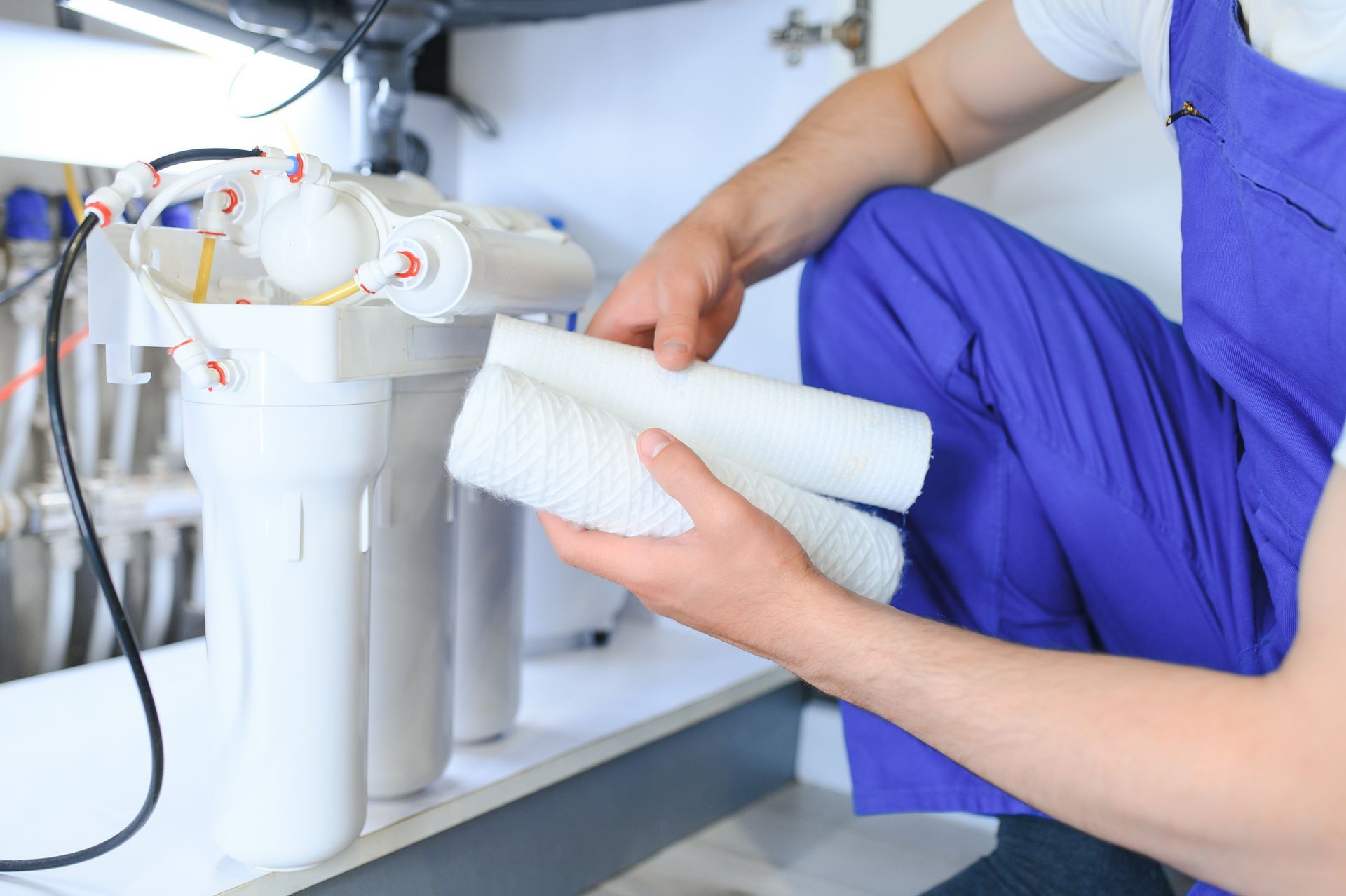Person installing a white water filter cartridge under a sink, holding the filter beside the system