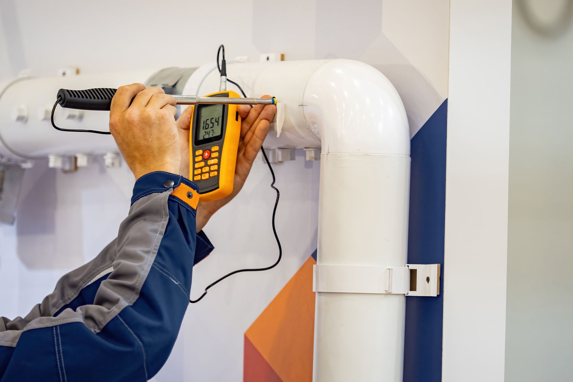 Technician using a handheld thermal camera to inspect white piping on a wall