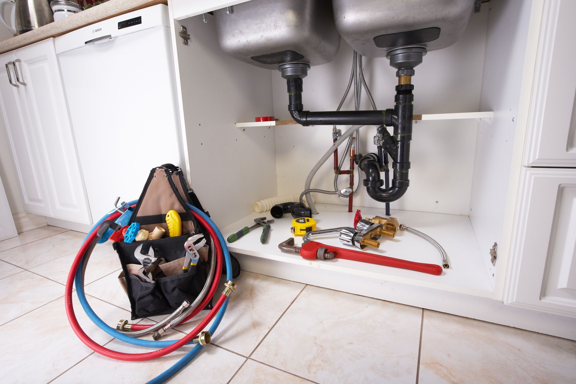 Under-sink plumbing repair setup with tools, hoses, and exposed pipes in a white cabinet