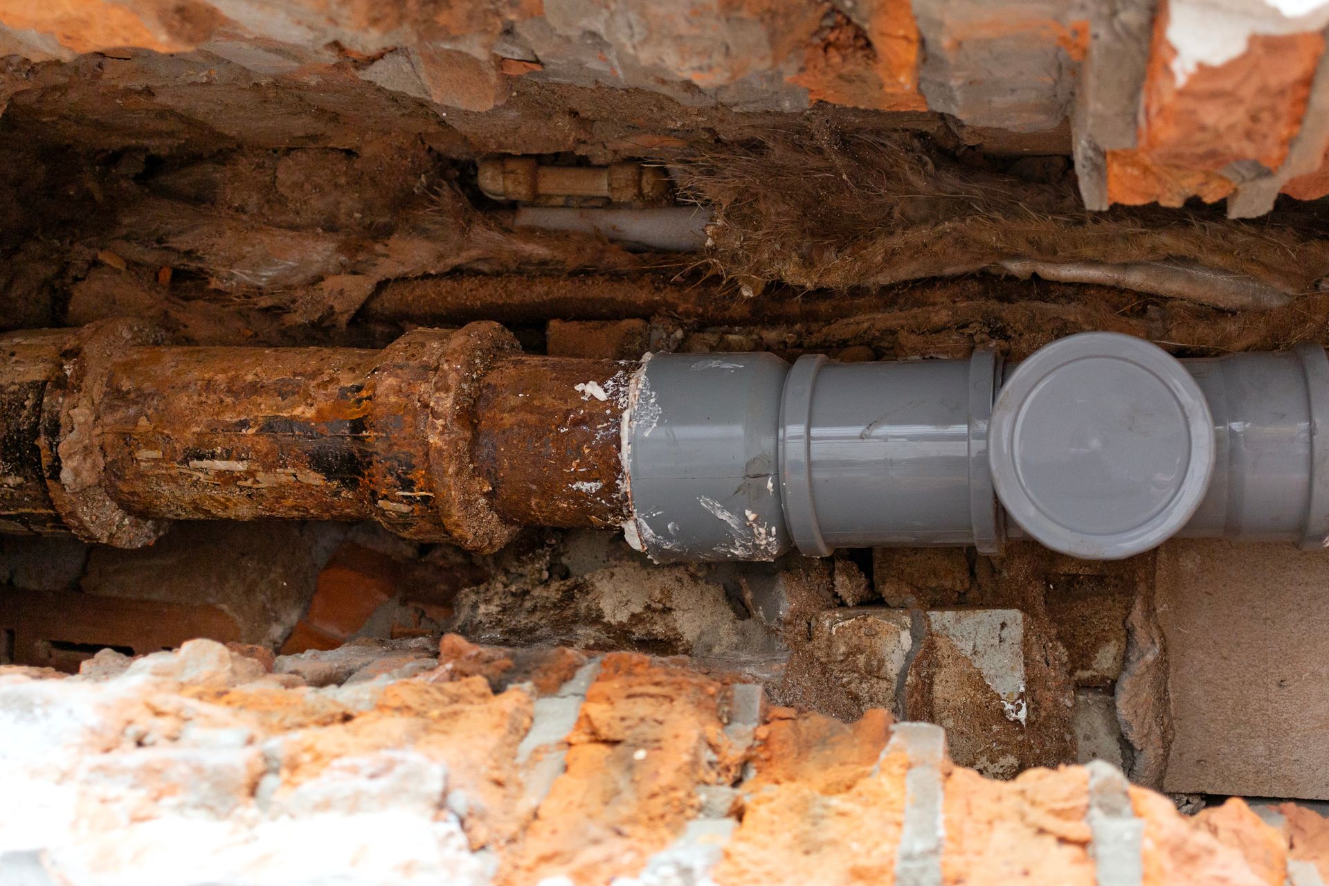 Gray sewer pipe in a dirt trench beneath a torn-up roadway, showing underground repair work
