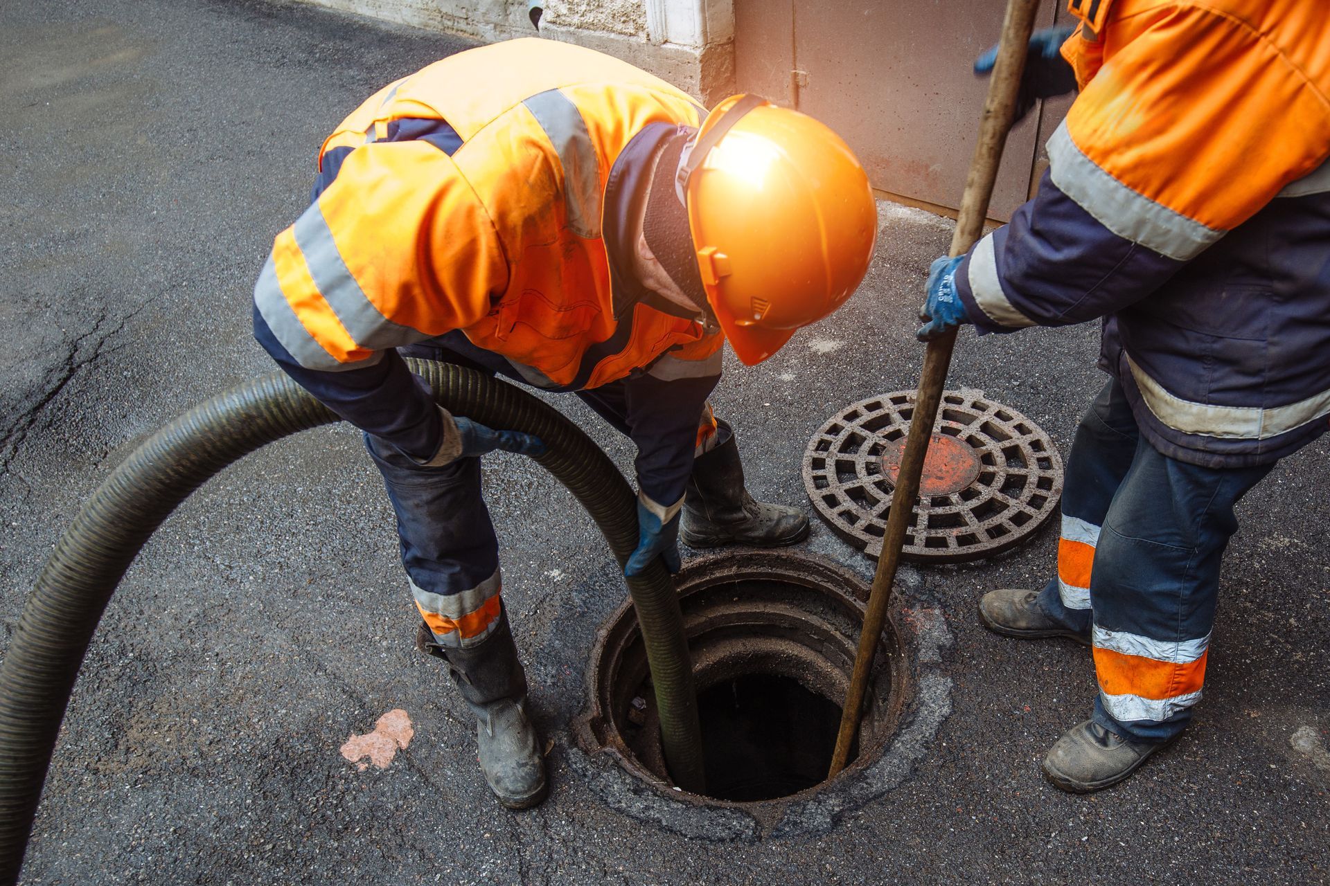Workers in orange safety gear inspecting a manhole on a wet road