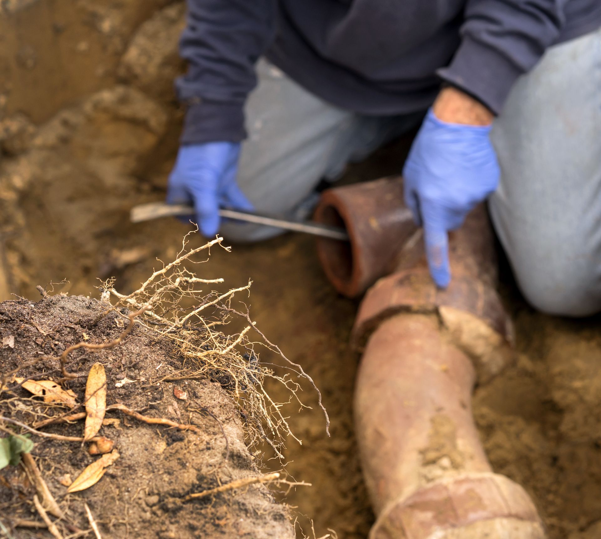 Gloved worker excavating and handling an old buried pipe in a muddy trench