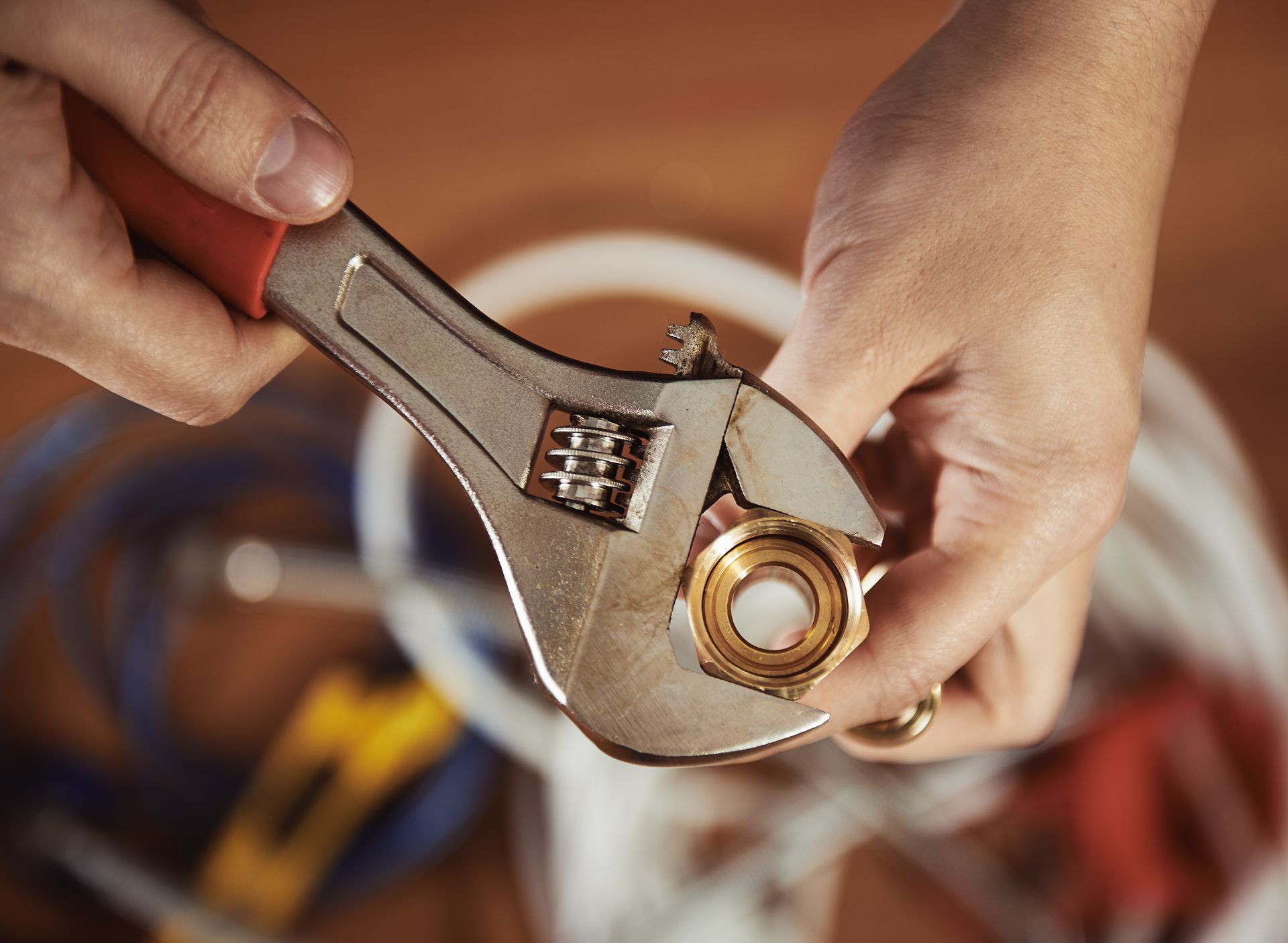 Hands using an adjustable wrench to tighten a brass fitting on a pipe.